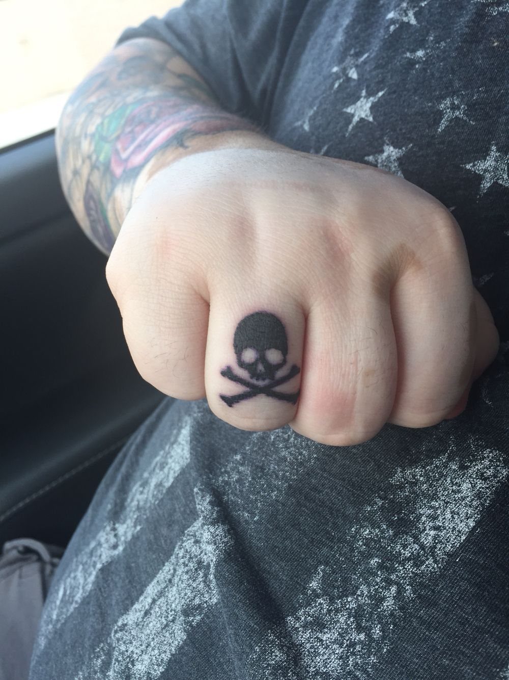 A small black skull and crossbones tattoo on a person's finger.