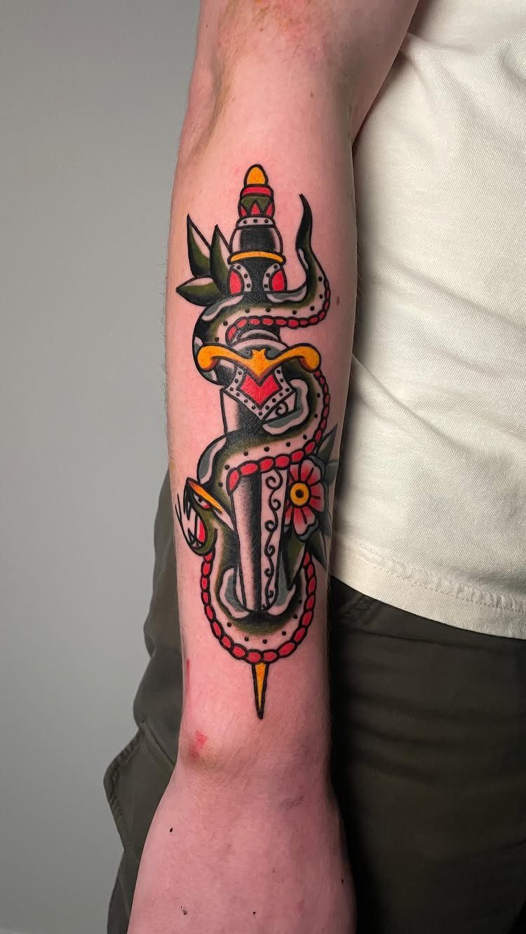 A colorful traditional tattoo of a snake wrapped around a dagger on a person's forearm.