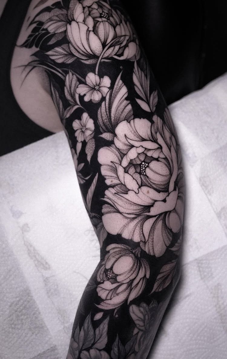 Large black ink floral tattoo with detailed peonies and leaves covering a person's arm.