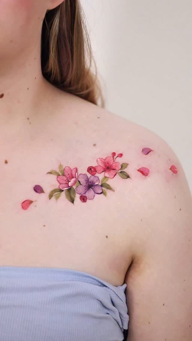Watercolor style floral tattoo with pink and purple blossoms on a person's shoulder.