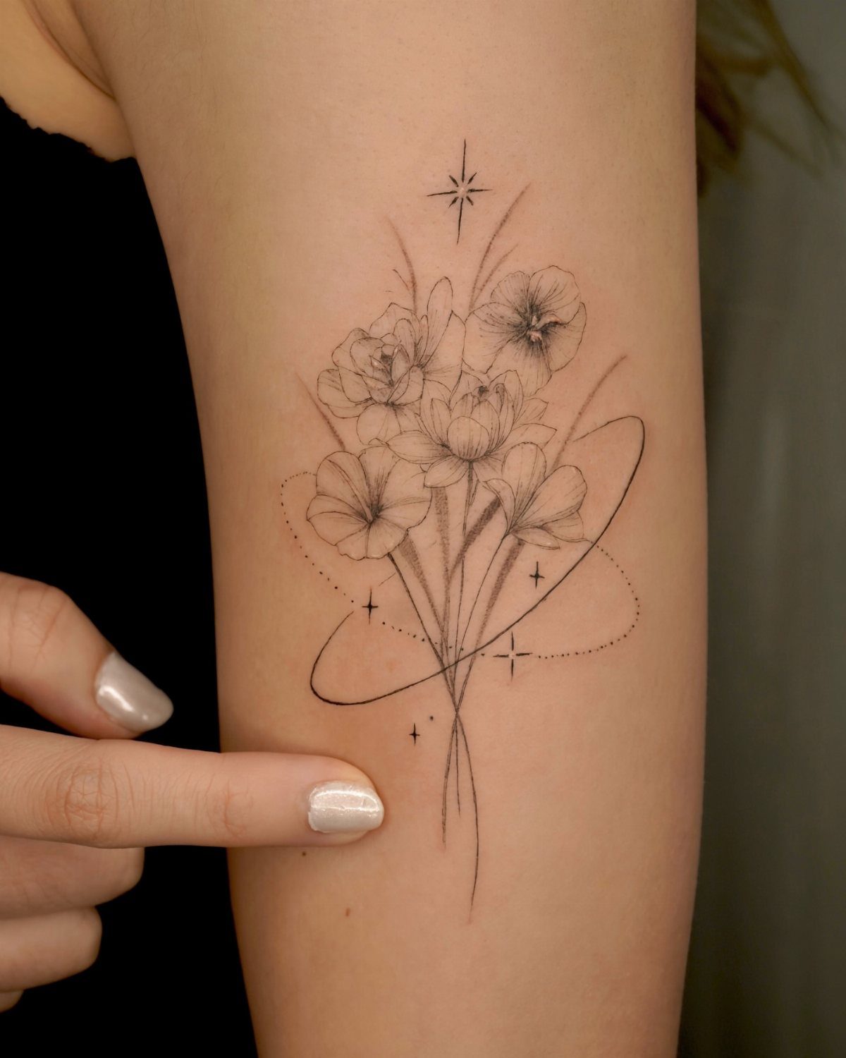 Fine-line floral bouquet tattoo with delicate outlines and small stars on a person's arm.