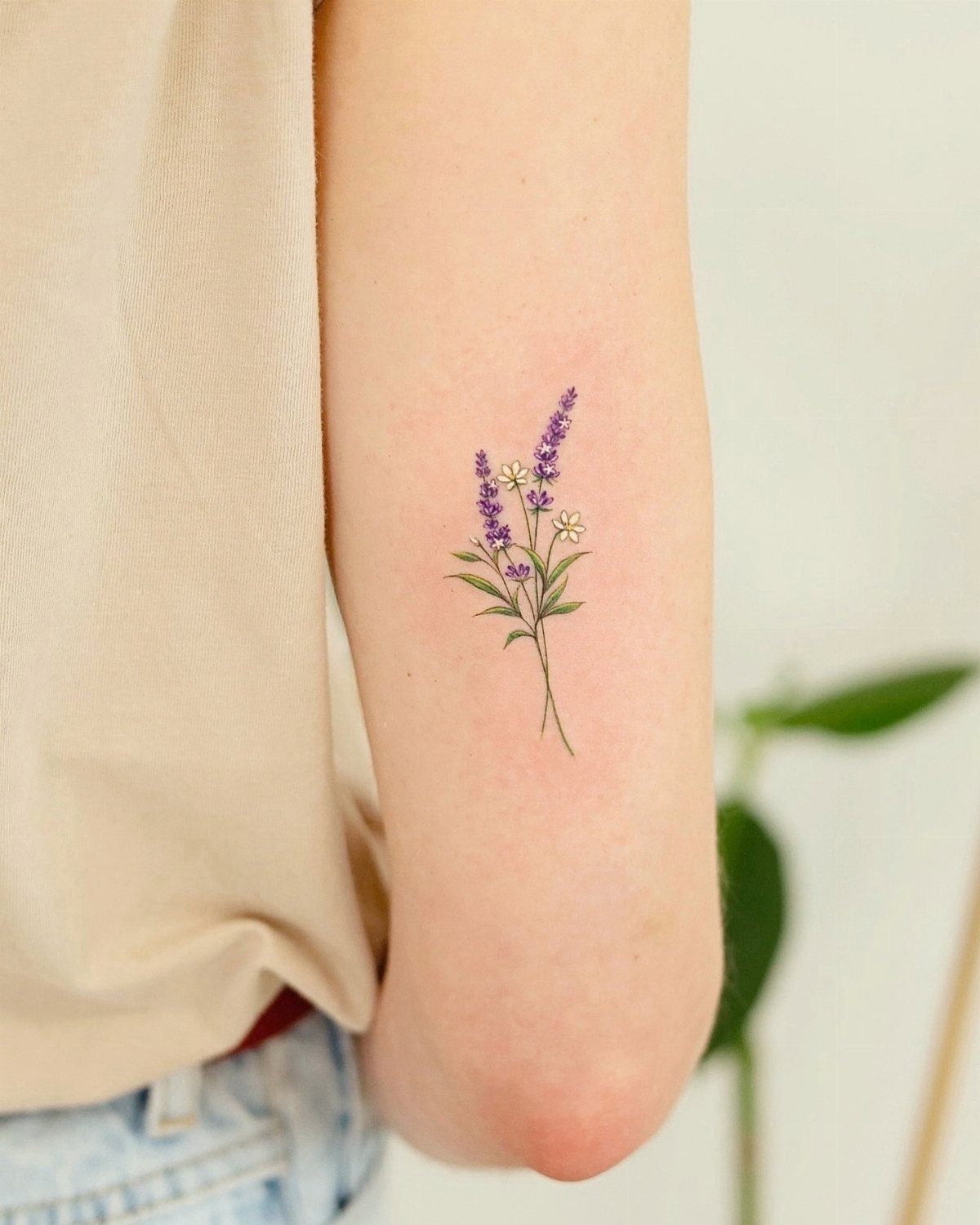 A small lavender and daisy floral tattoo on a person's arm.