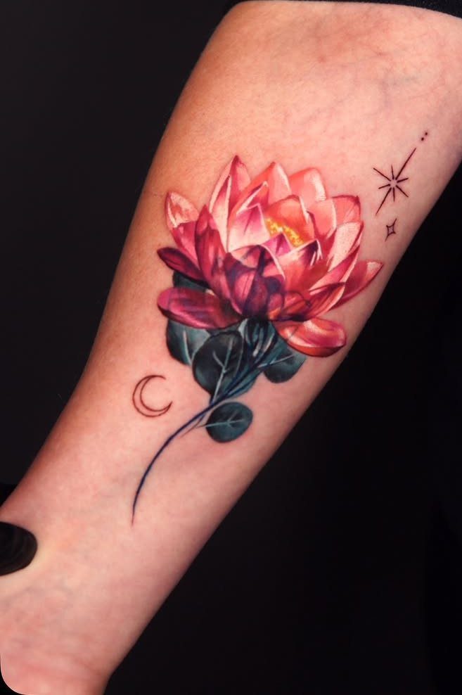 A vibrant pink and orange lotus flower tattoo with leaves and stars on an arm.