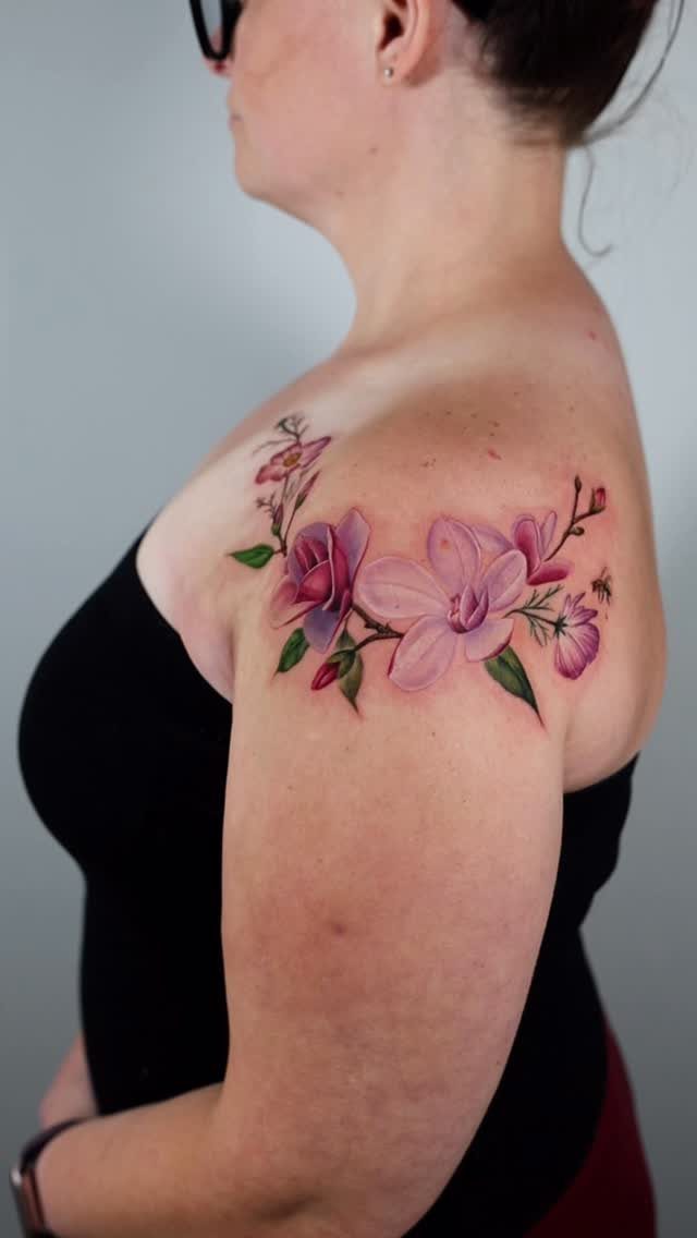 A pink magnolia flower tattoo with green leaves on a person's shoulder.