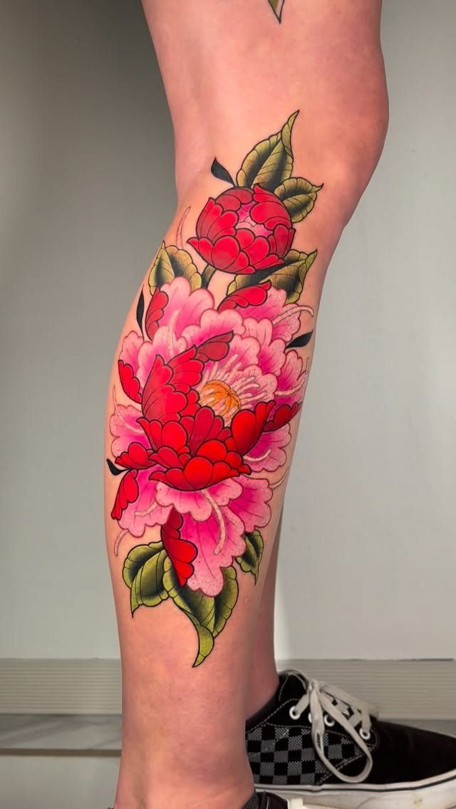A large pink and red peony flower tattoo on a person's lower leg.