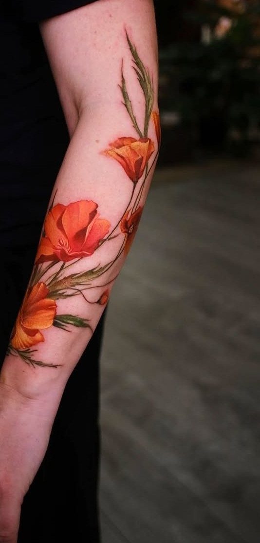 A vibrant orange poppy flower tattoo winding around a person's forearm with green leaves.