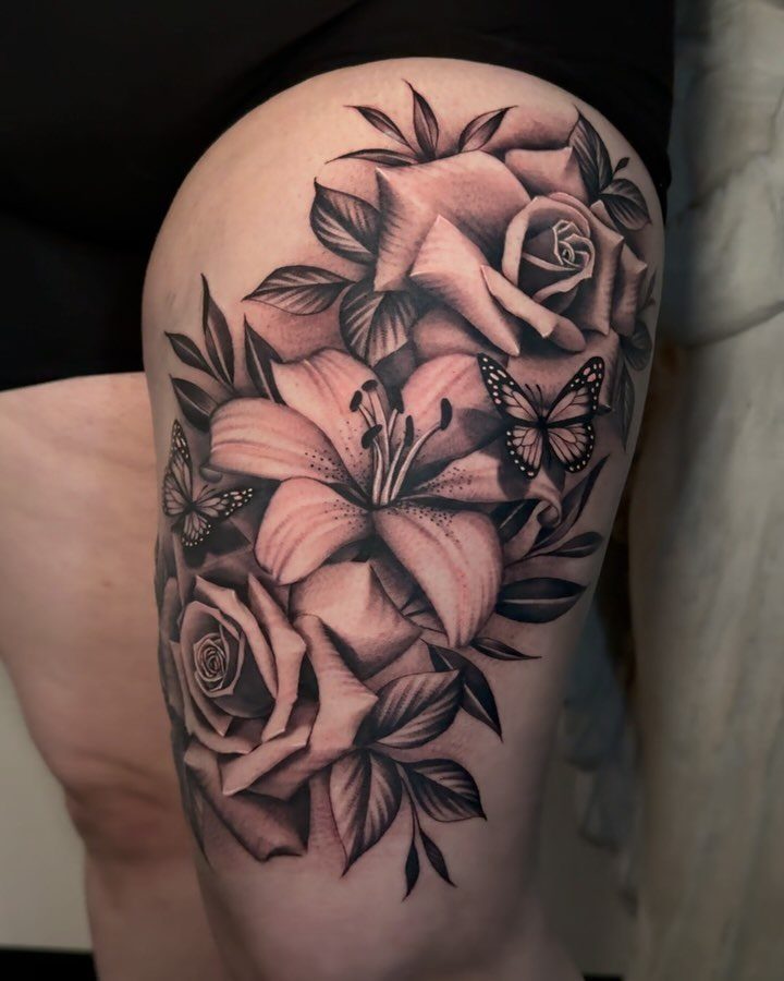 Black and grey floral tattoo on a thigh featuring roses, a lily, and butterflies.