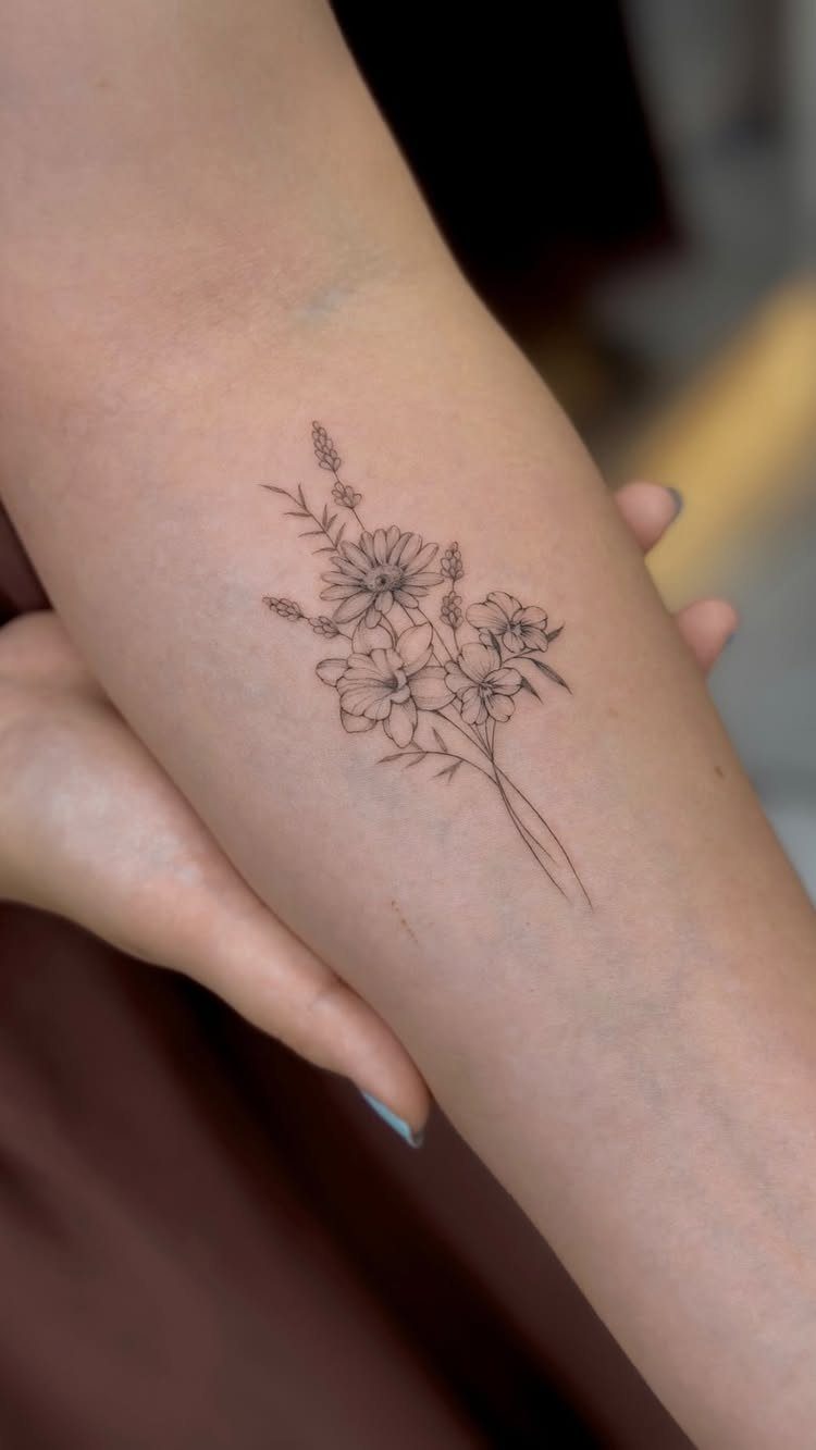 Fine-line black ink tattoo of a small wildflower bouquet on a person's forearm.