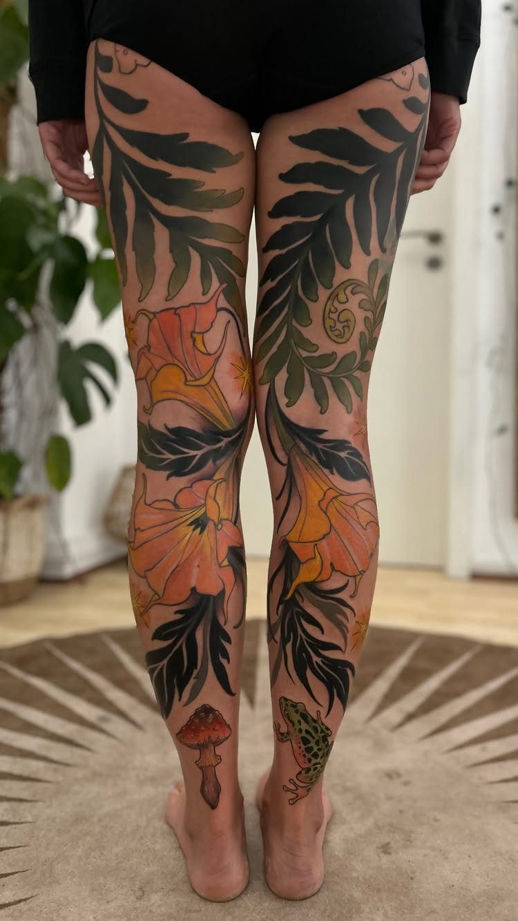 Large colorful leg tattoos featuring orange flowers, green leaves, and a small green frog near the ankle.