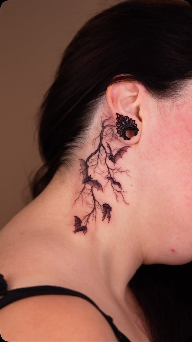 A black ink tattoo of flying bats and branches on a person's neck.