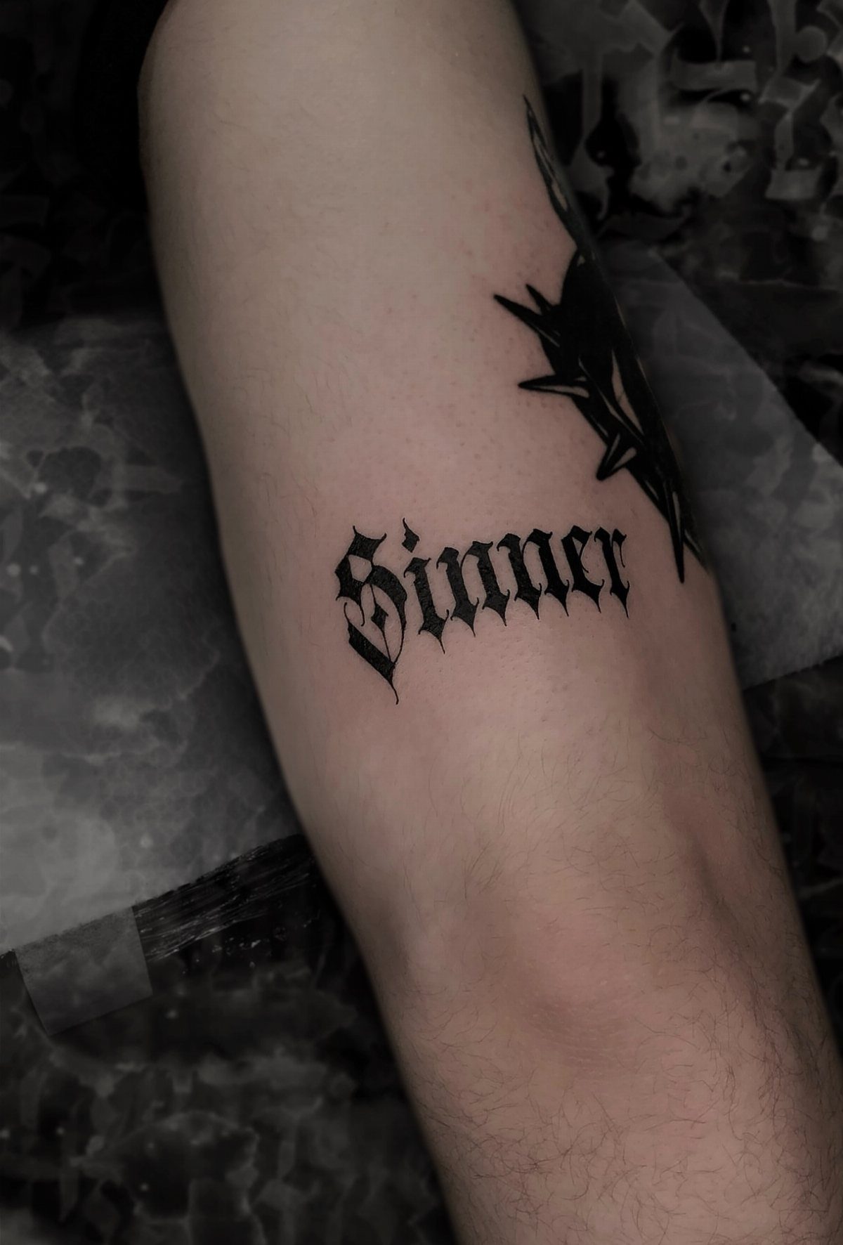 A blackletter gothic font tattoo reading Sinner on a person's arm.