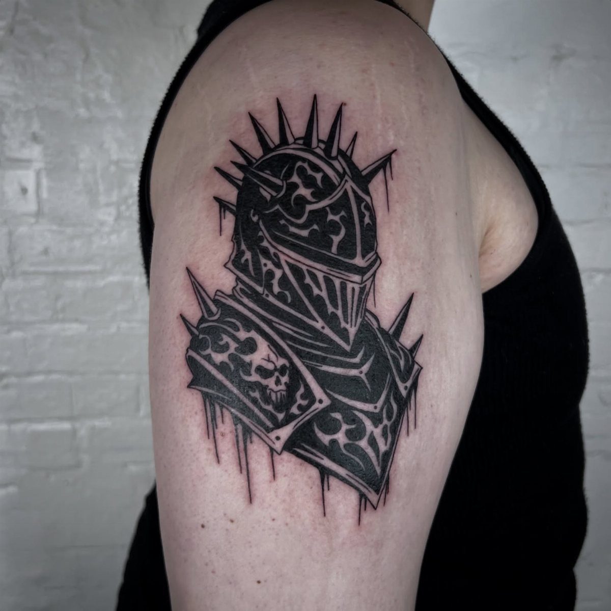 A black ink gothic knight helmet tattoo on a person's upper arm.