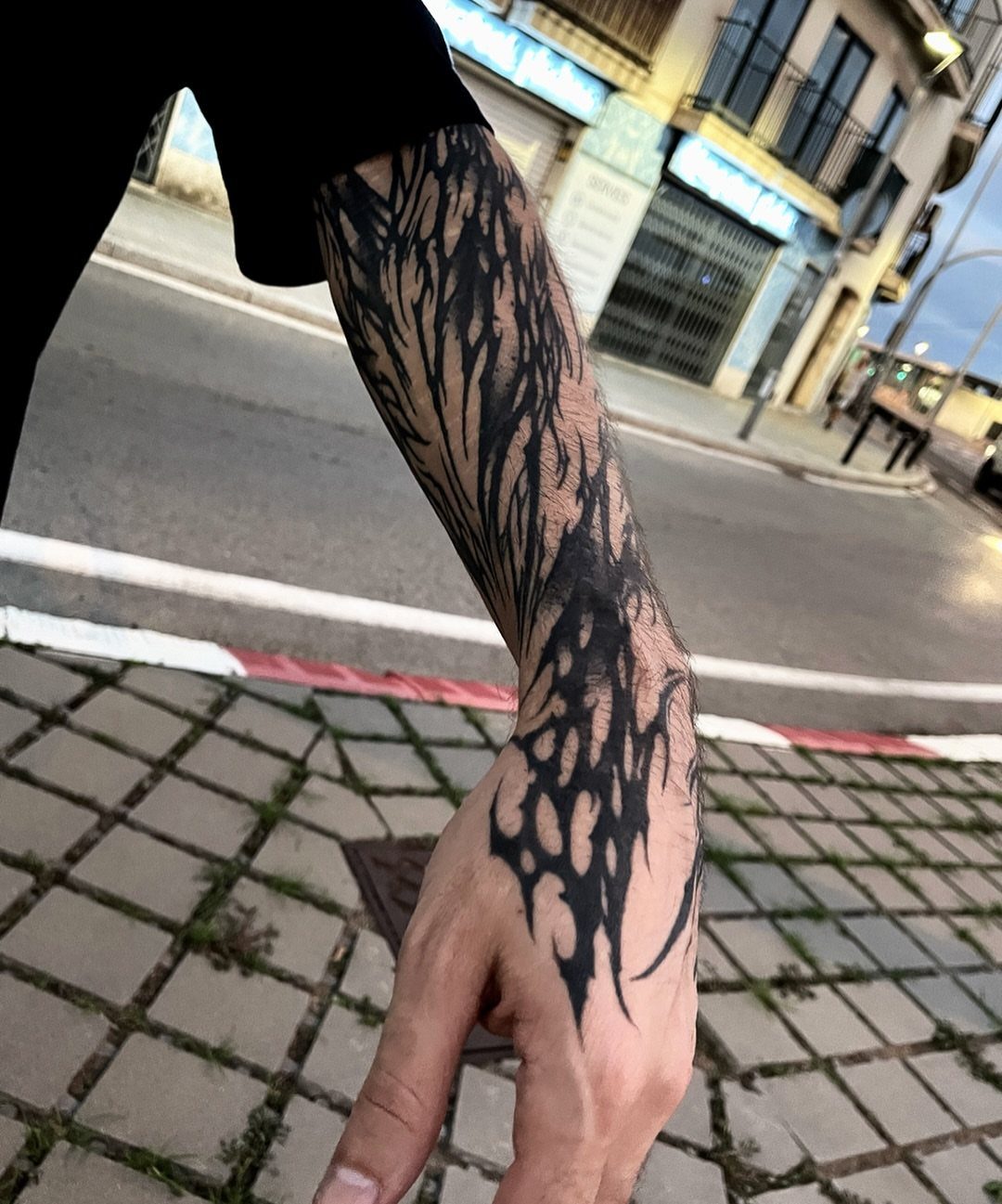 A person's arm and hand covered in a large, black tribal pattern tattoo.