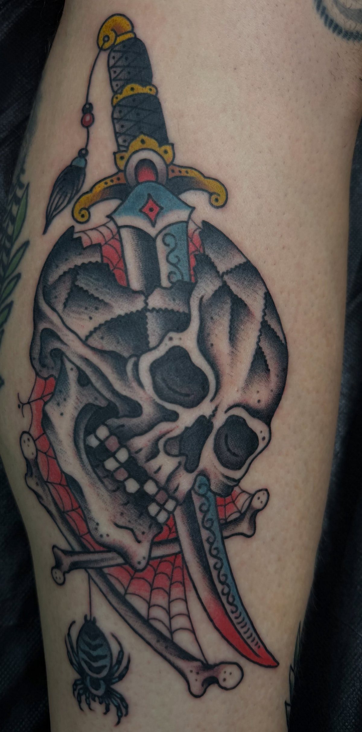 7 Leg Tattoo Ideas for Women: Geometric, Floral, Fine Line & More 7 A skull pierced by a dagger tattoo with a spider and web design on a leg.
