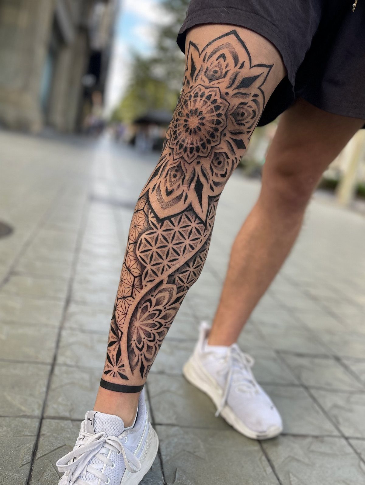 7 Leg Tattoo Ideas for Women: Geometric, Floral, Fine Line & More 1 A person's leg displaying a large, intricate black ink mandala and geometric pattern tattoo.