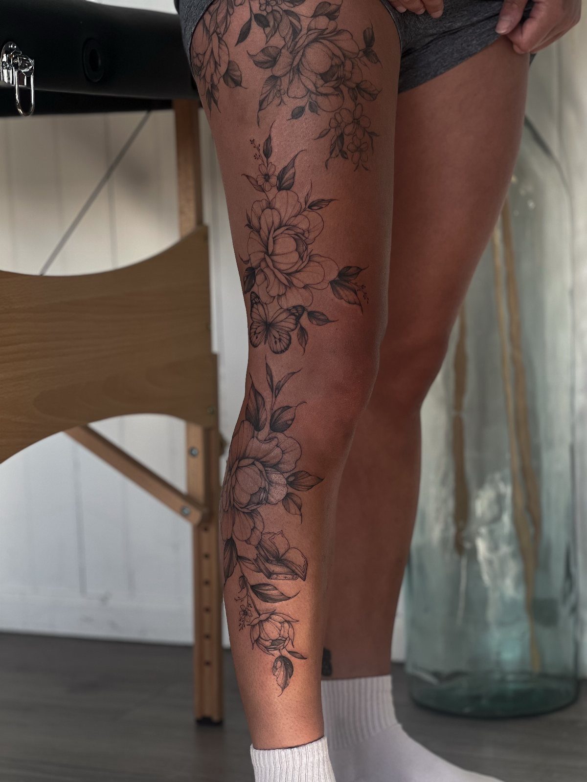 7 Leg Tattoo Ideas for Women: Geometric, Floral, Fine Line & More 2 A large black ink floral tattoo covering a person's entire leg from thigh to ankle.