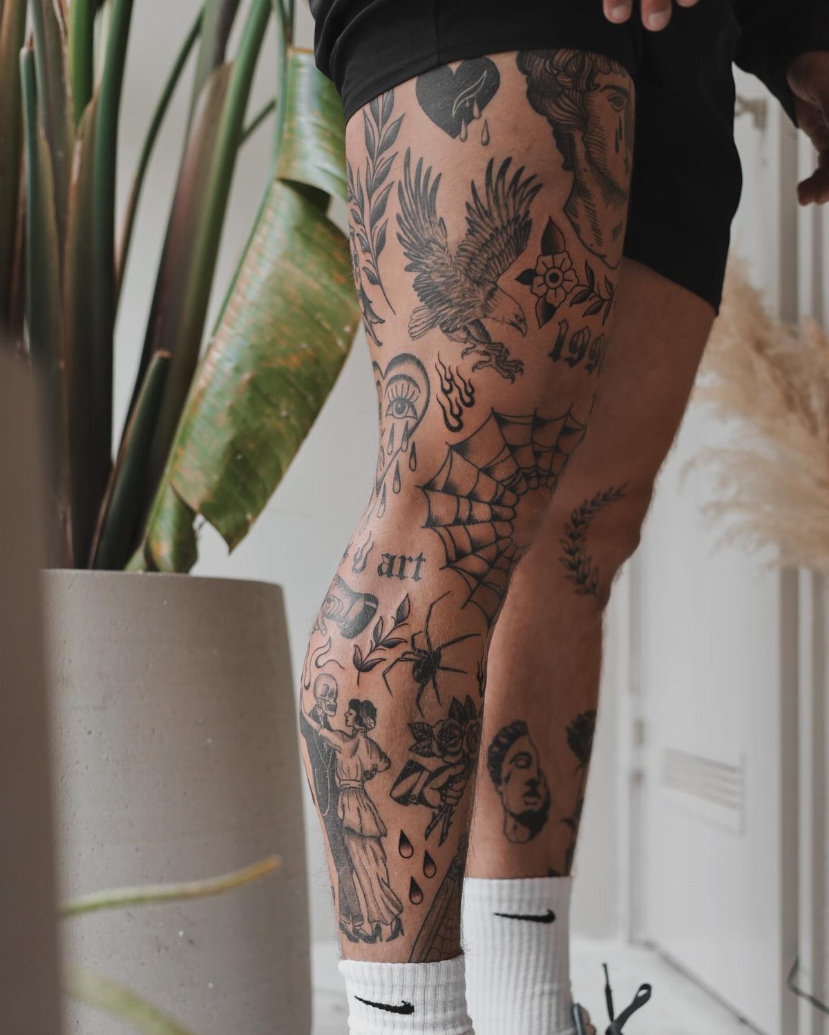 7 Leg Tattoo Ideas for Women: Geometric, Floral, Fine Line & More 5 A person's leg featuring multiple black ink patchwork style tattoos including an eagle and spider web.