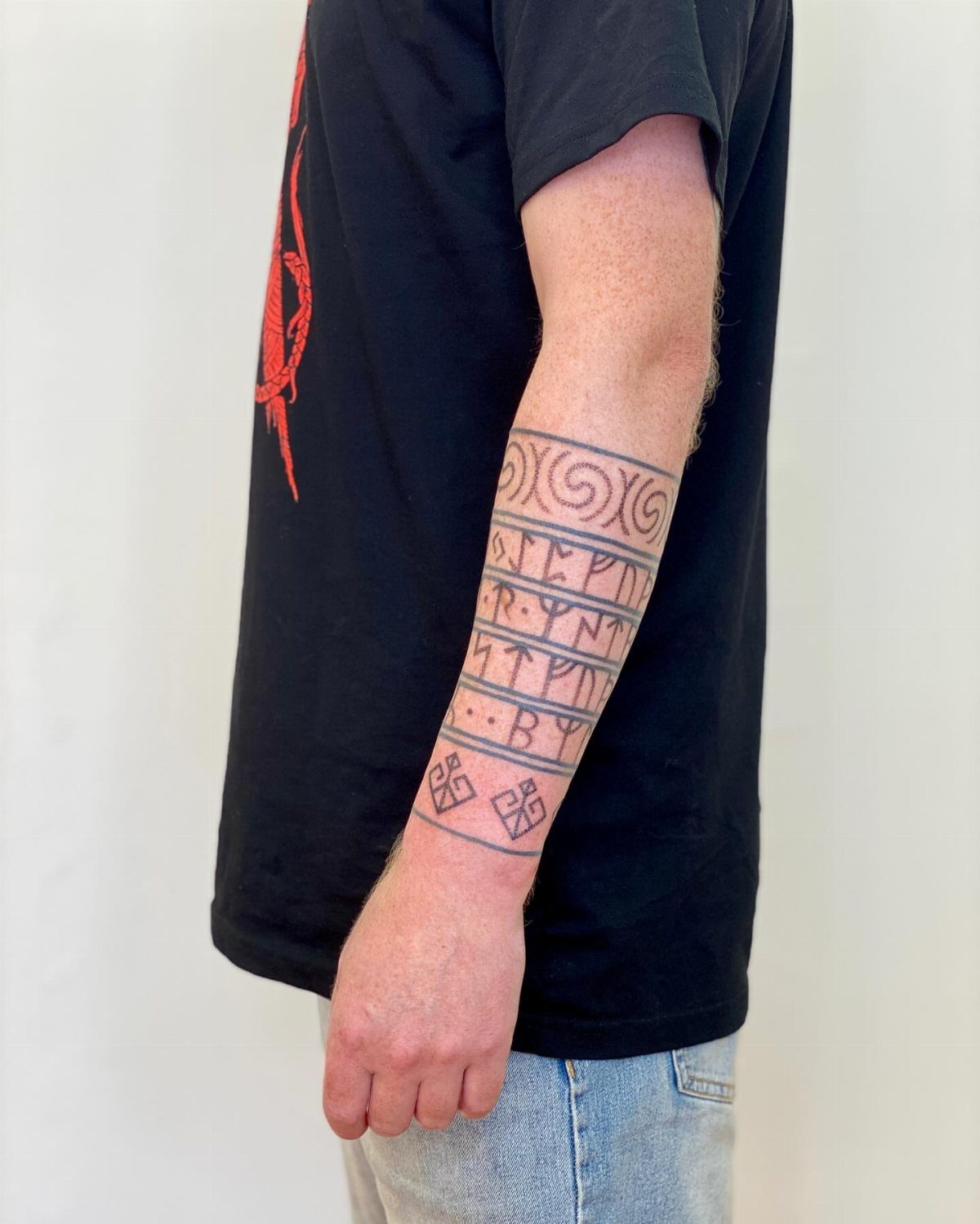 Nordic Runes Tattoo: 10 Design Ideas Worth Considering 5 A forearm tattoo featuring black ink Nordic runes and geometric patterns arranged in horizontal bands.