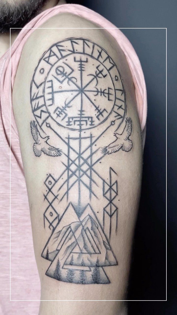 Nordic Runes Tattoo: 10 Design Ideas Worth Considering 3 A large black ink tattoo on an arm featuring runes, geometric patterns, birds, and mountains.