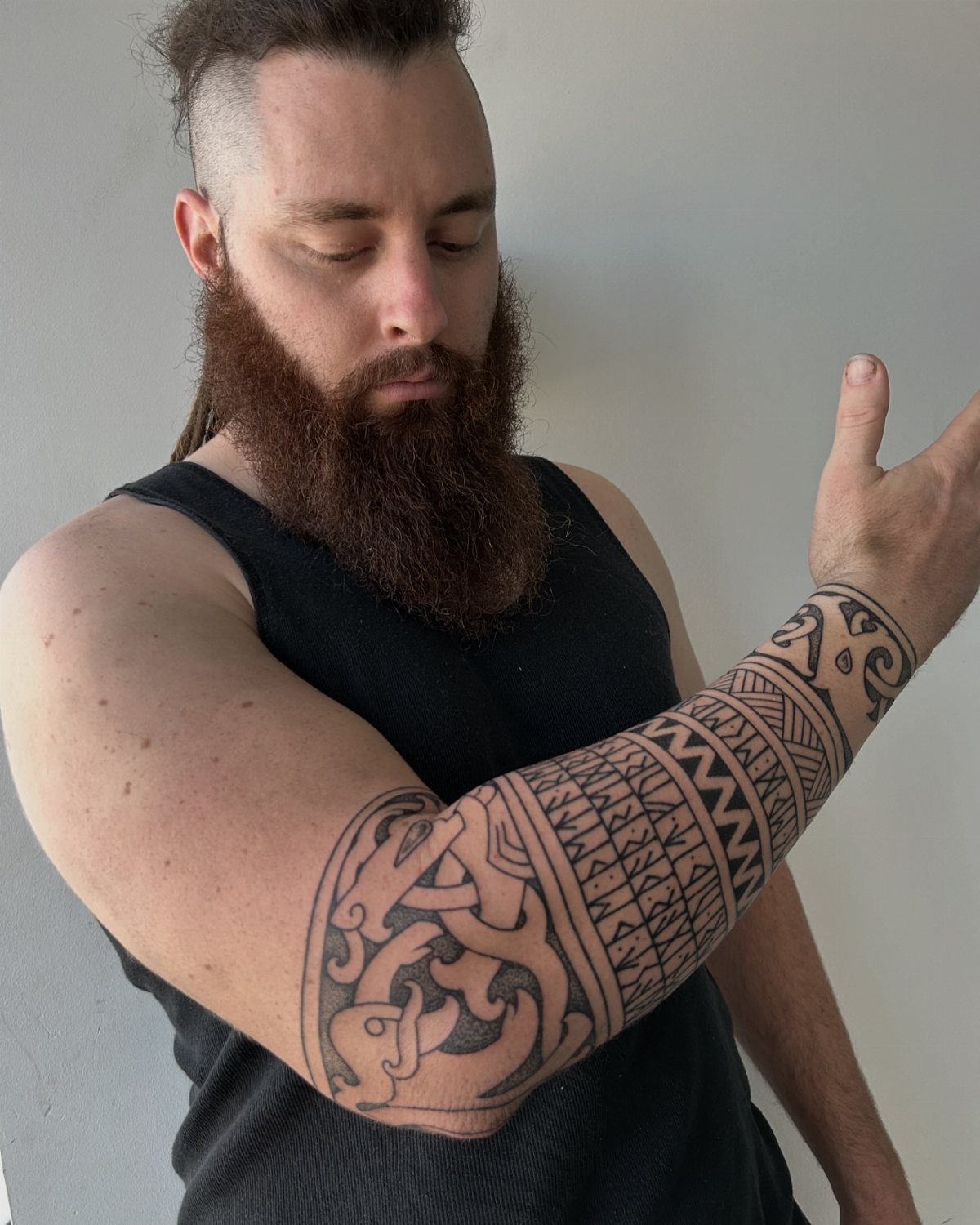 Nordic Runes Tattoo: 10 Design Ideas Worth Considering 7 A man with a red beard displaying a large black ink Nordic knotwork tattoo on his forearm.