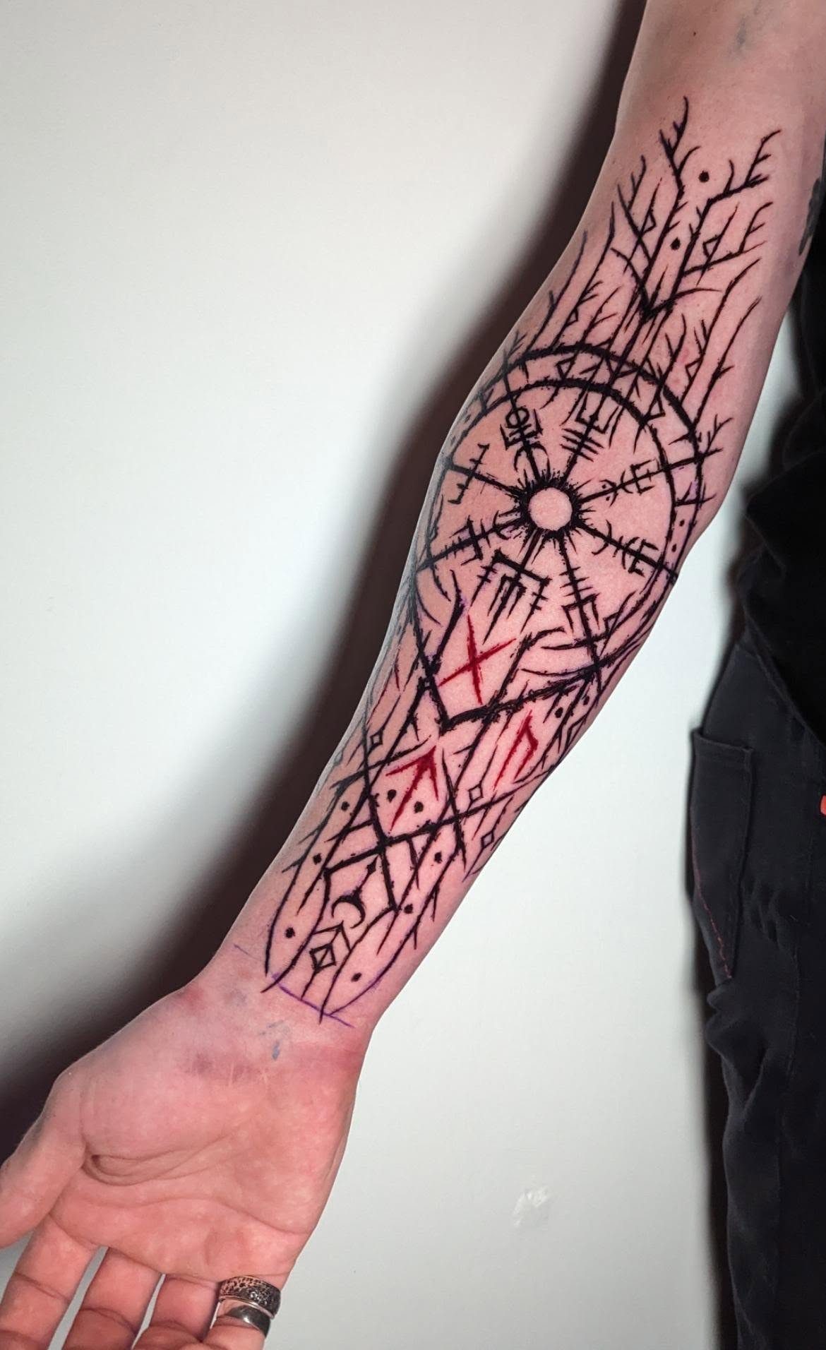 Nordic Runes Tattoo: 10 Design Ideas Worth Considering 4 A large black ink forearm tattoo featuring geometric patterns and runic symbols with red accents.
