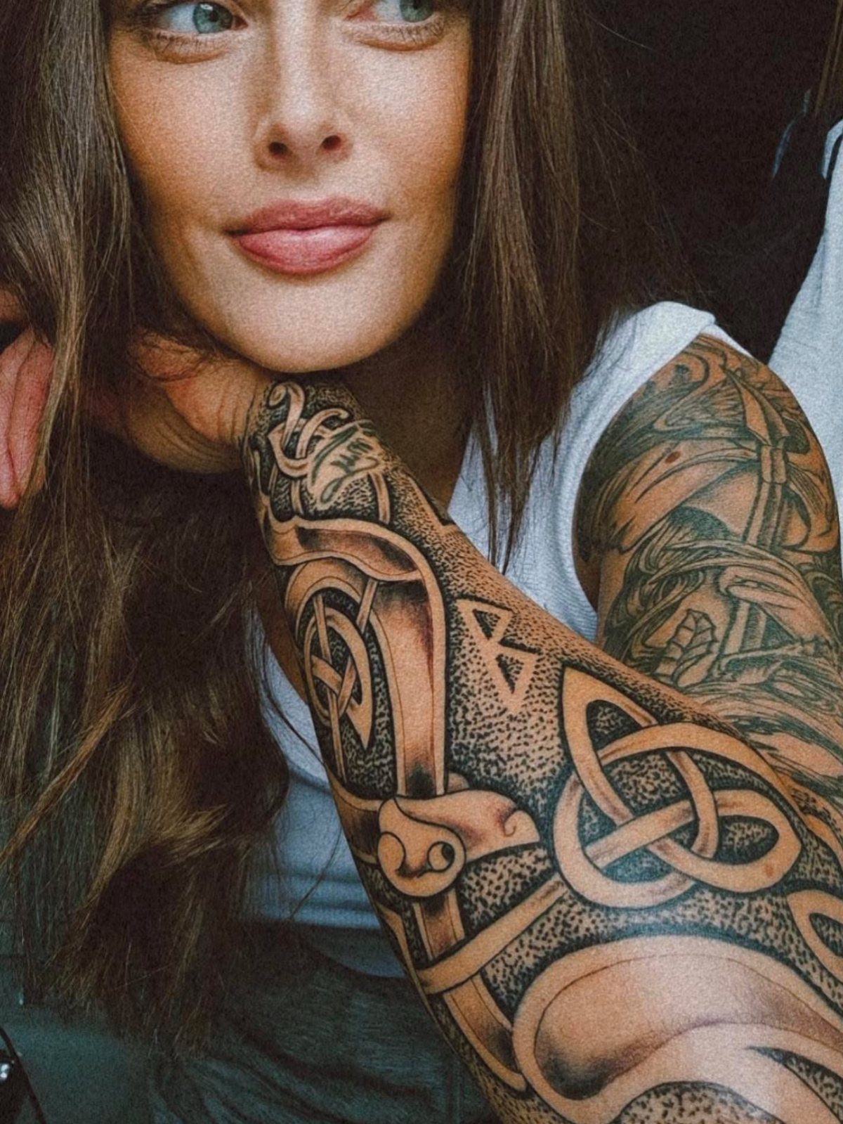 Nordic Runes Tattoo: 10 Design Ideas Worth Considering 9 A woman's arm displaying a large, detailed black and grey Nordic rune and knotwork tattoo.