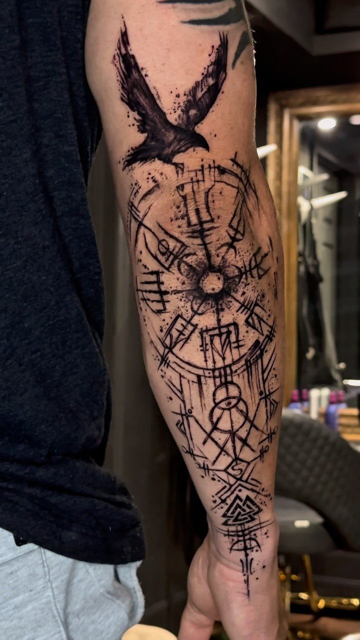 Nordic Runes Tattoo: 10 Design Ideas Worth Considering 10 A large black ink forearm tattoo featuring a raven above intricate geometric runic symbols.