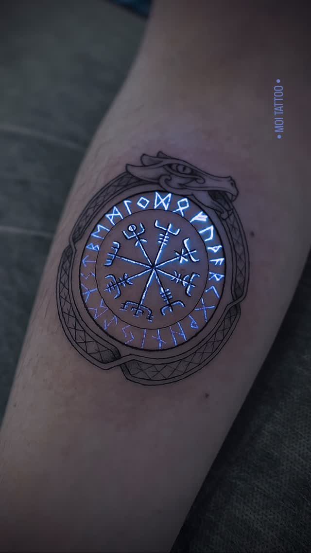 Nordic Runes Tattoo: 10 Design Ideas Worth Considering 2 A glowing blue Vegvisir compass tattoo on a person's forearm with intricate black ink details.