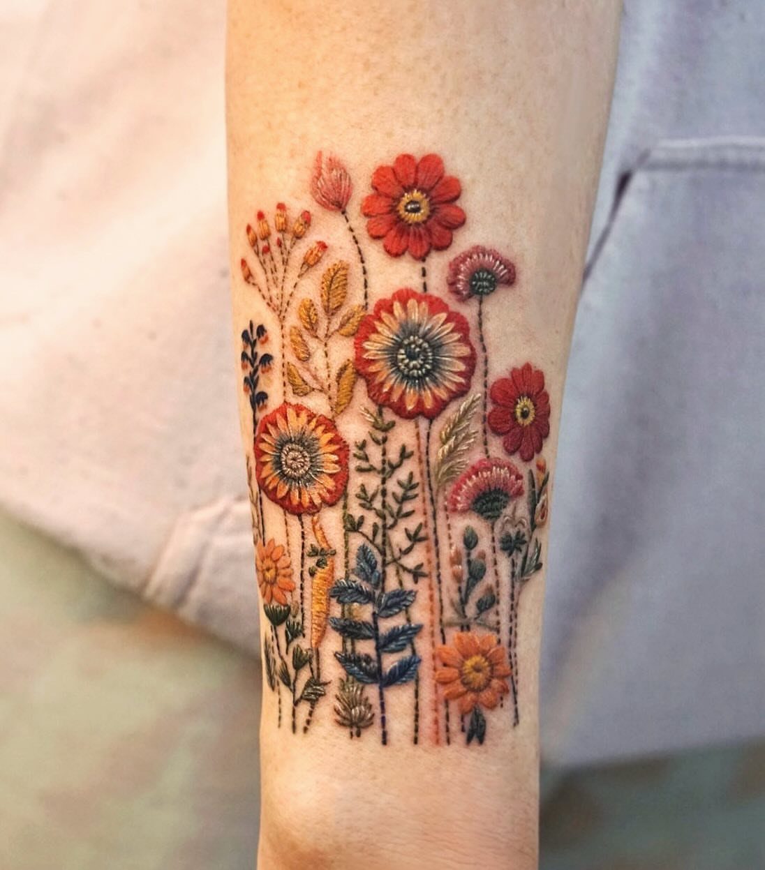 A detailed floral tattoo with colorful embroidered-style wildflowers on a person's forearm.