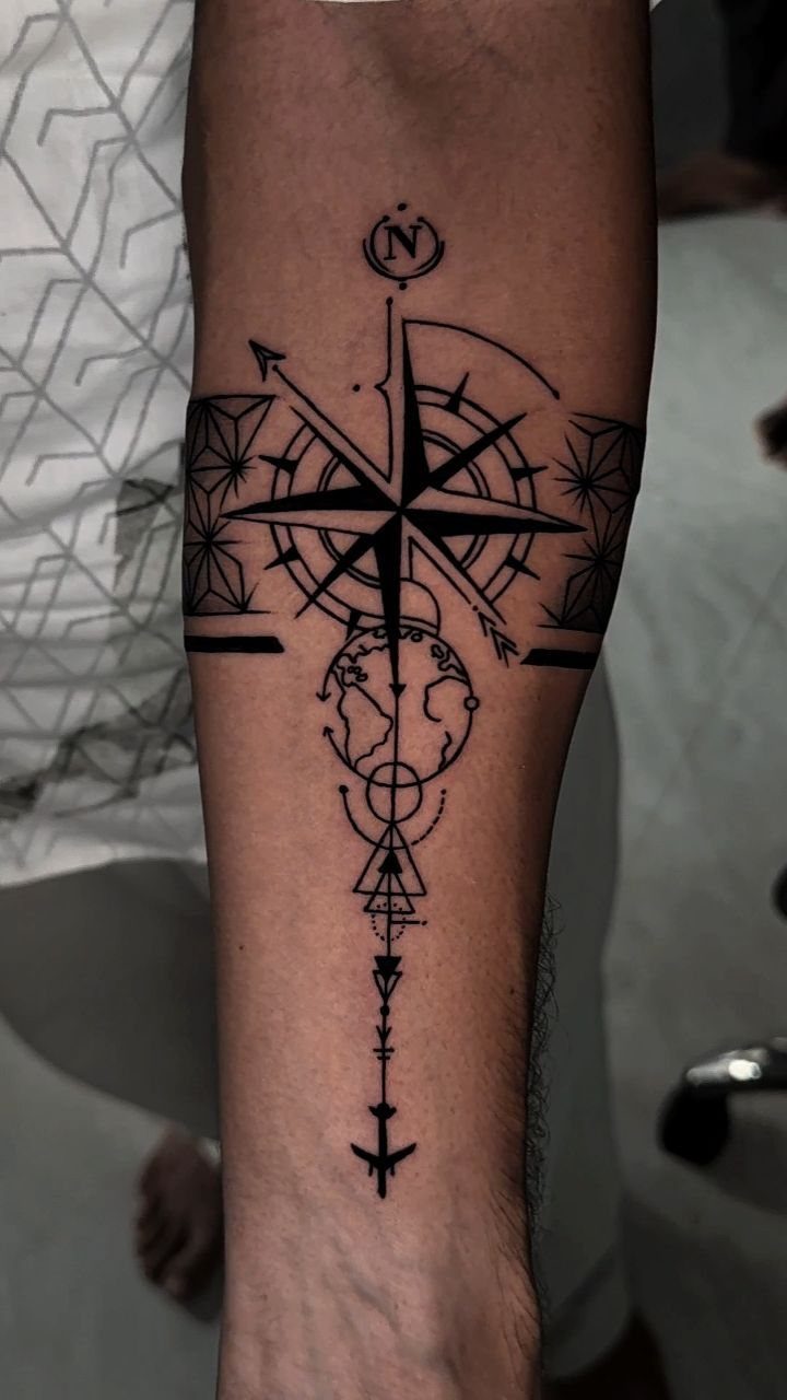 A black ink forearm tattoo featuring a compass rose, a globe, and geometric line work.