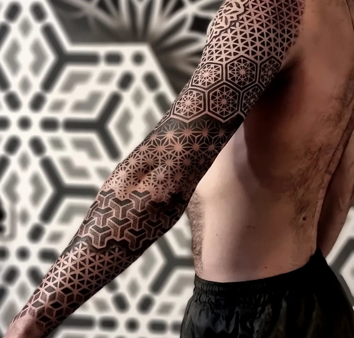 A man's arm covered in a detailed black ink geometric pattern tattoo sleeve.