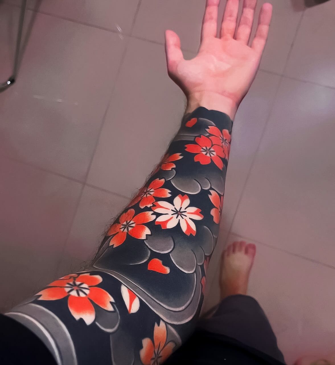 A person's arm displaying a large tattoo of orange and white cherry blossoms on a dark background.