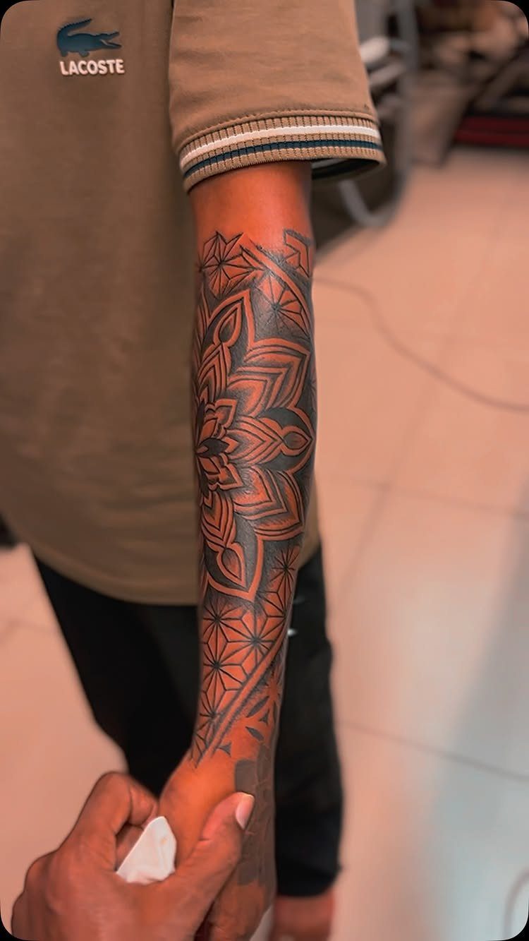 A detailed black ink mandala pattern tattoo covering a person's entire forearm.