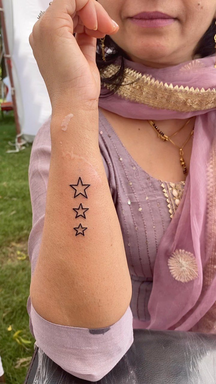 Three small black outline stars tattooed vertically on a person's forearm.