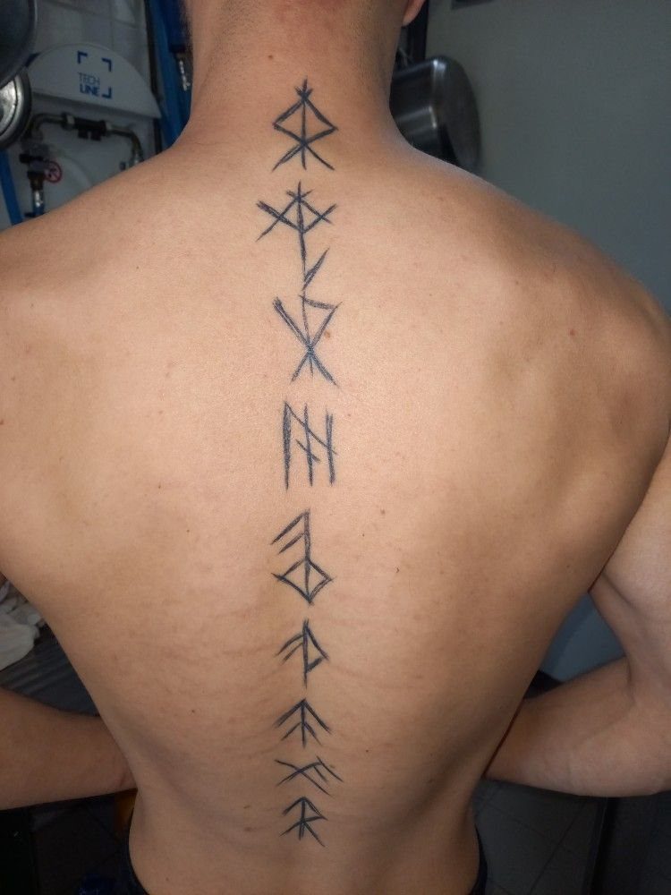 Rune Tattoo Ideas: 18 Symbols and Placements Worth Studying 7 A vertical column of black rune tattoos running down a person's bare back.