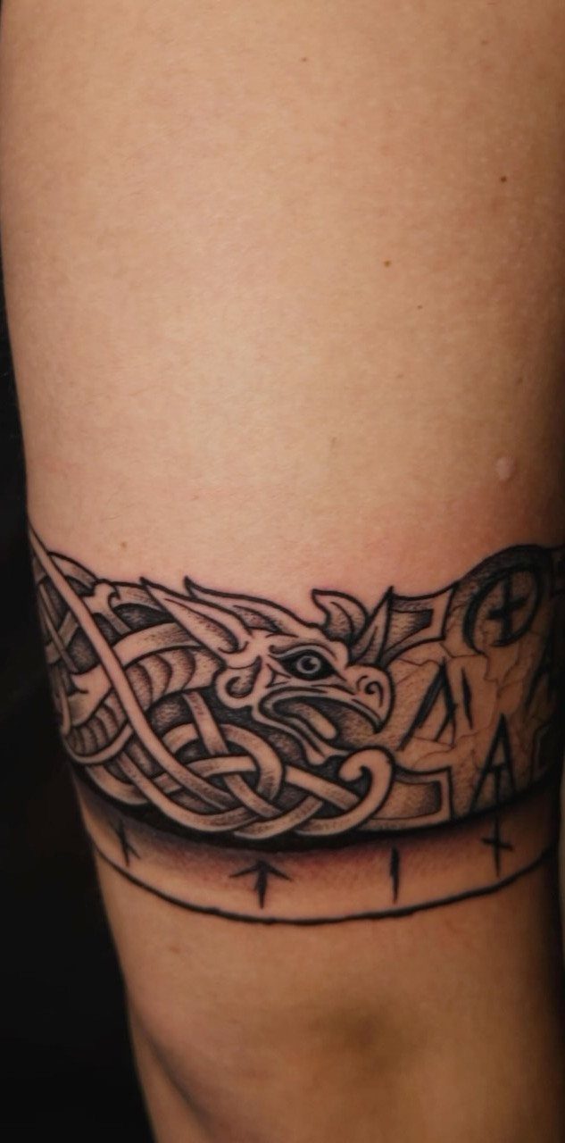 Rune Tattoo Ideas: 18 Symbols and Placements Worth Studying 4 A black and grey band tattoo with Celtic knotwork and runes on a person's arm.