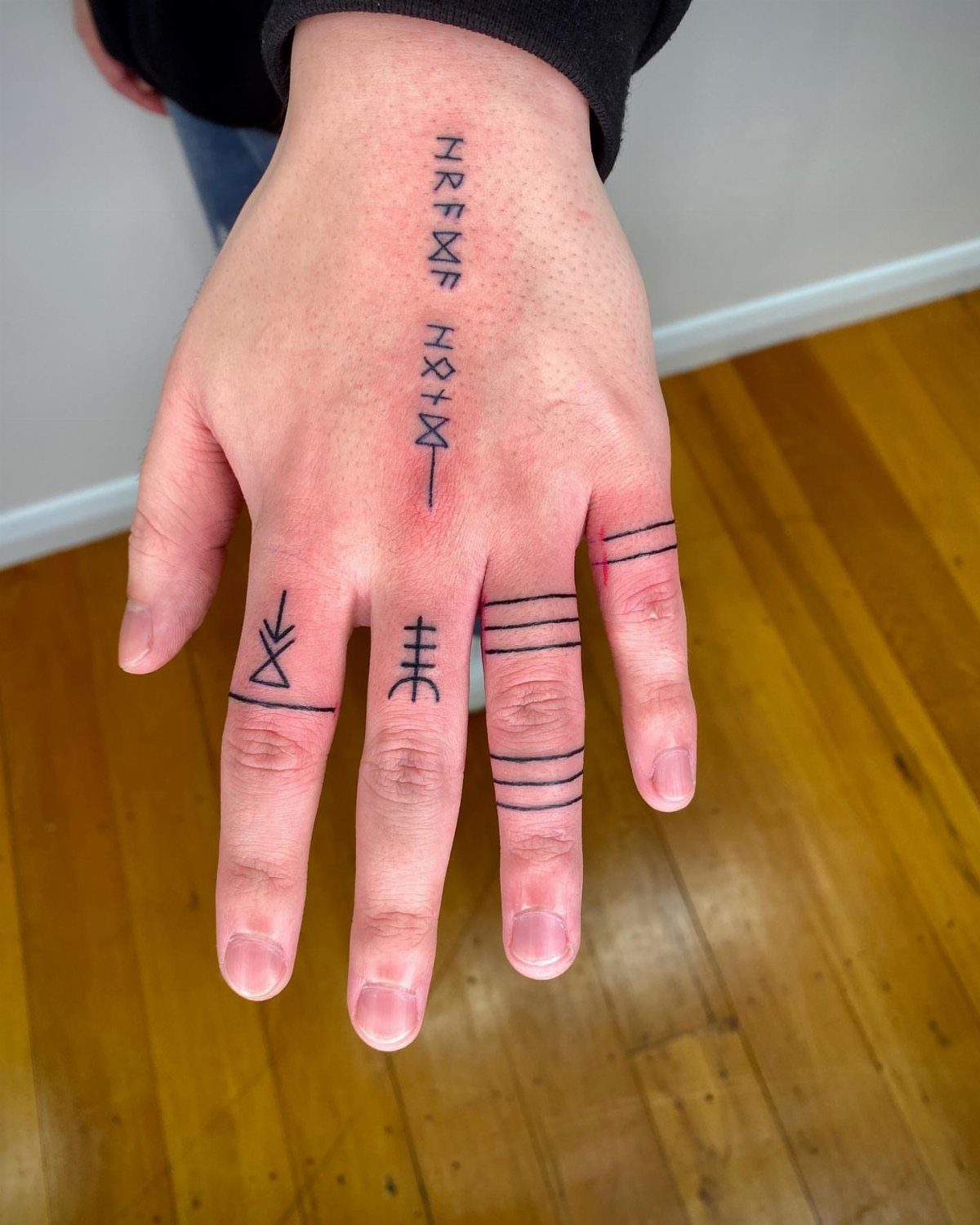 Rune Tattoo Ideas: 18 Symbols and Placements Worth Studying 10 A hand with various black ink rune tattoos and horizontal bands on the fingers.
