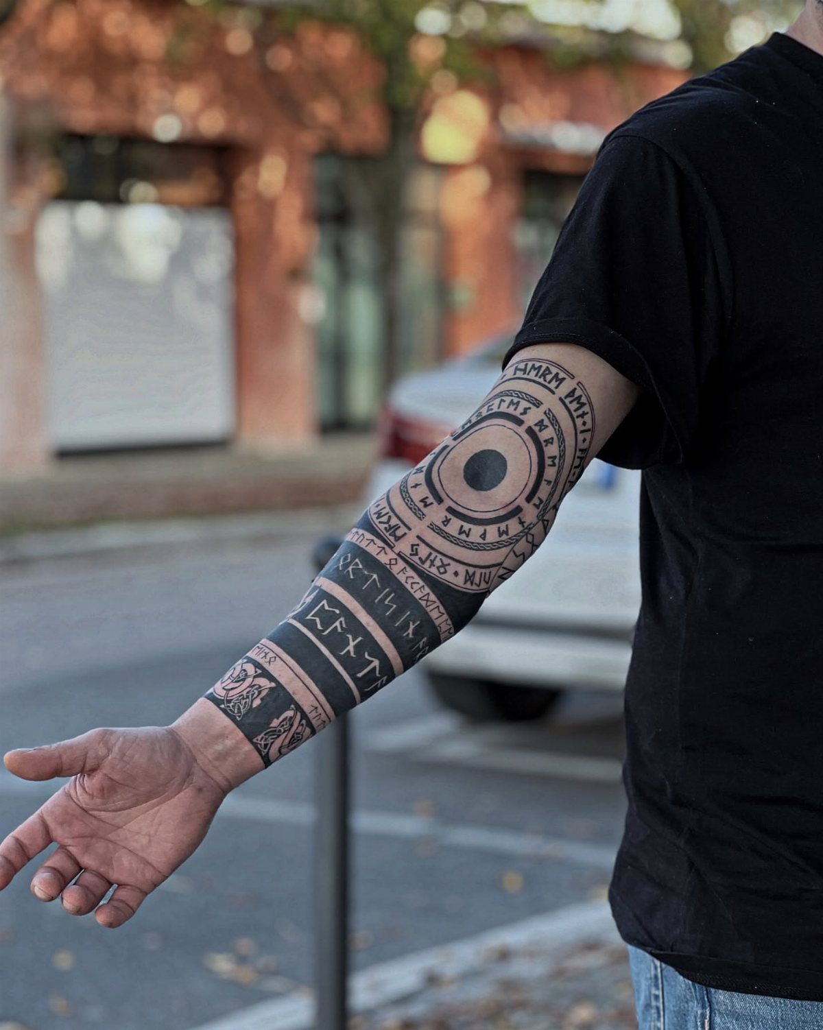 Rune Tattoo Ideas: 18 Symbols and Placements Worth Studying 5 A person's forearm displaying a large black ink tattoo with circular rune patterns and geometric bands.