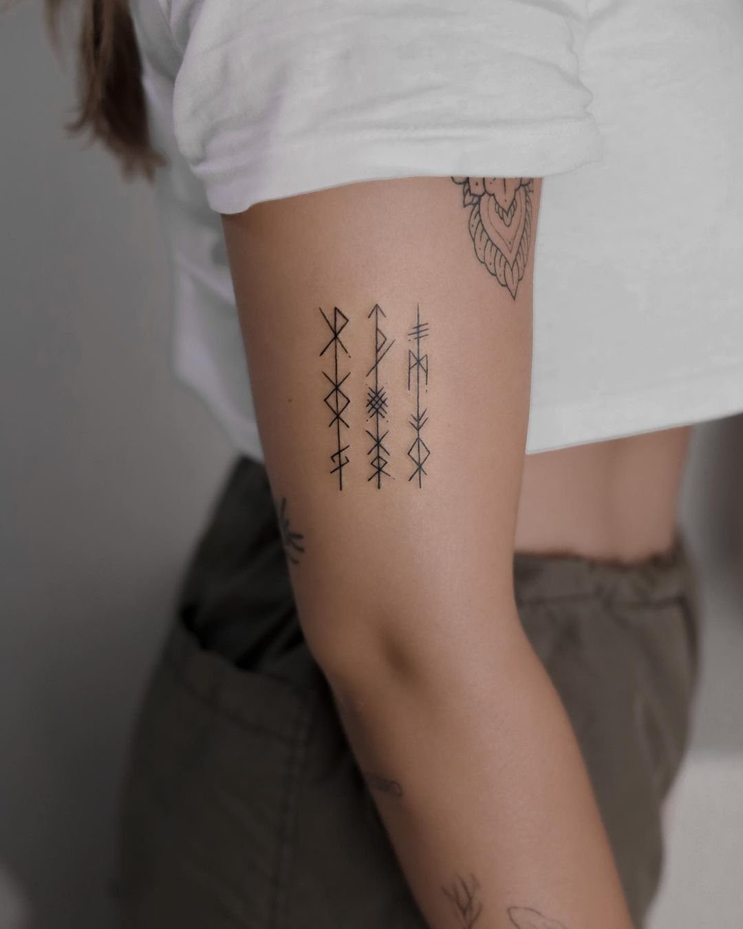 Rune Tattoo Ideas: 18 Symbols and Placements Worth Studying 11 A vertical tattoo of three black rune symbols on a person's upper arm.
