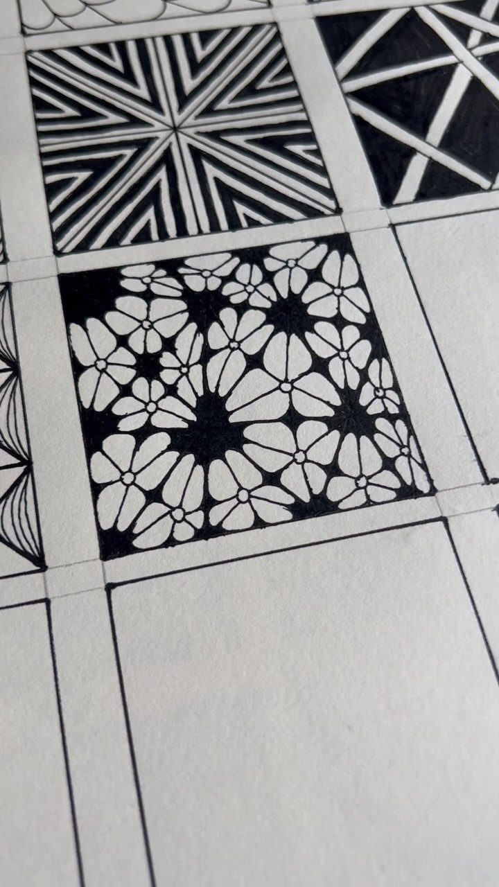Black ink drawing of various geometric and floral patterns contained within square grid panels on paper.