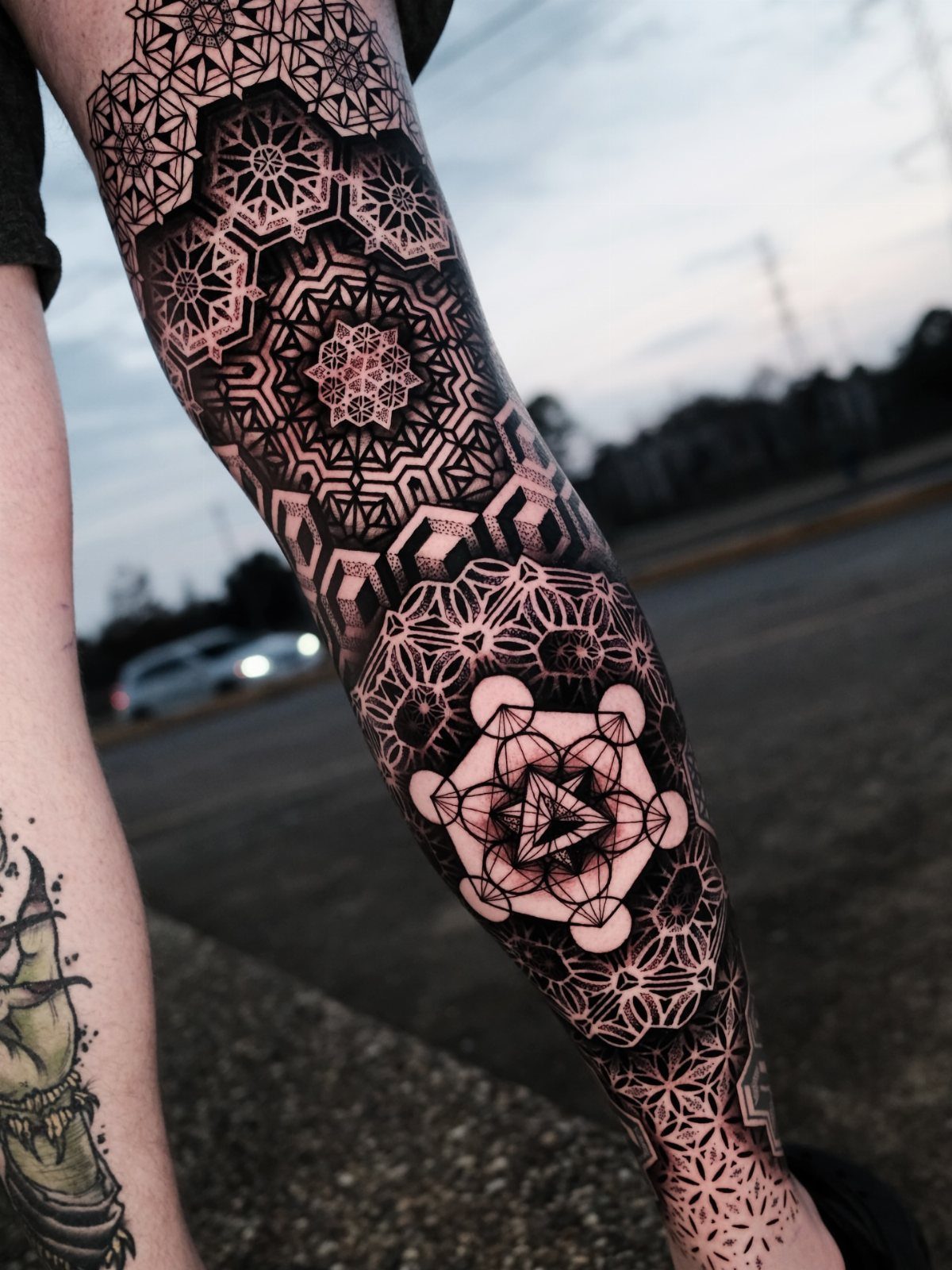 Intricate black ink sacred geometric tattoos covering a person's lower leg against an outdoor background.
