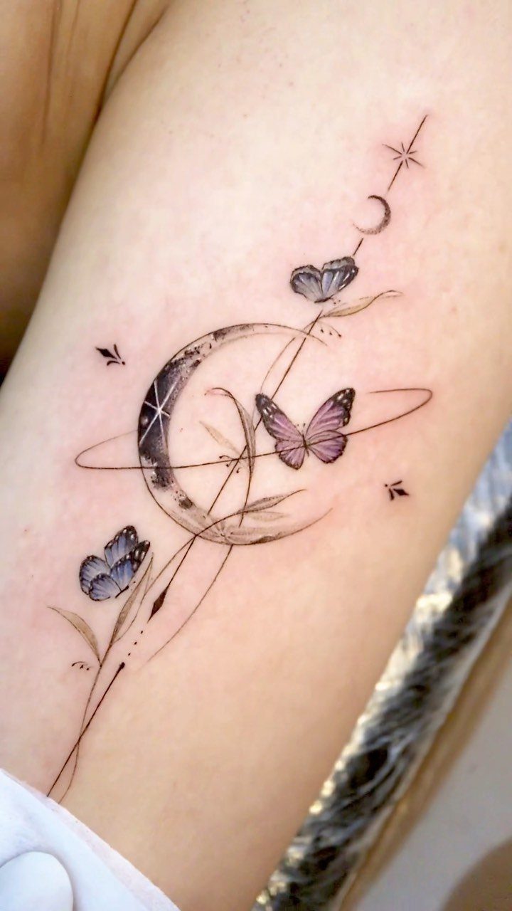 Fine line tattoo of purple butterflies, a crescent moon, and stars on a person's skin.