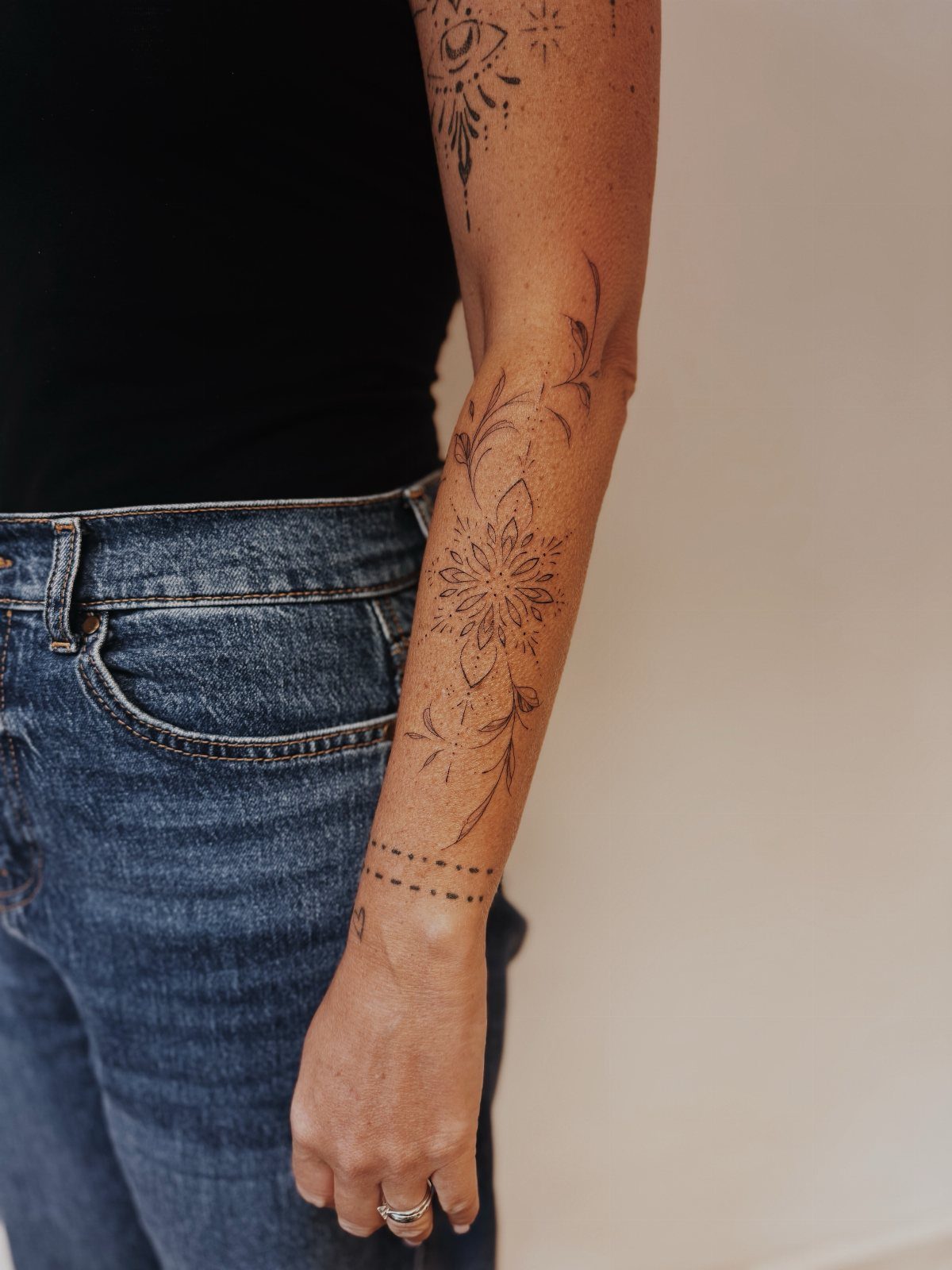 A person's arm displaying a detailed floral mandala tattoo and other black ink designs.