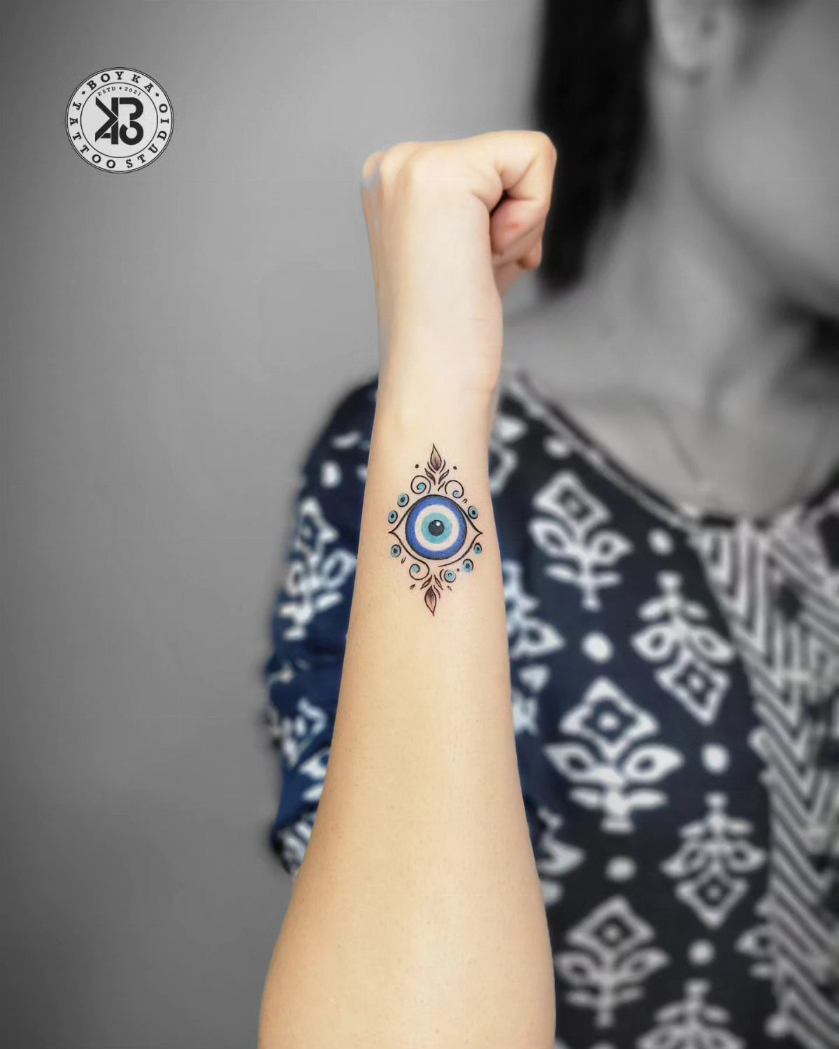 A small blue evil eye tattoo on a person's inner forearm.