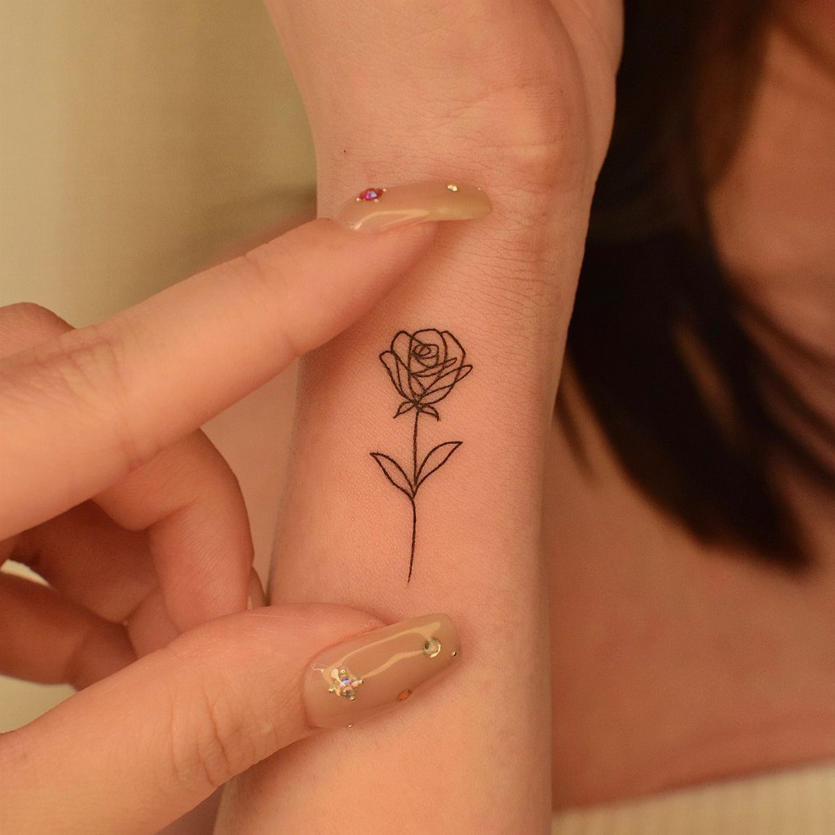A single rose fine-line tattoo on a person's inner wrist with manicured nails.