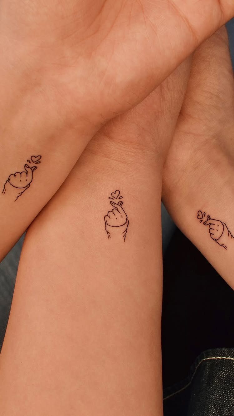 Three wrists displaying small minimalist finger heart tattoos with tiny hearts in black ink.