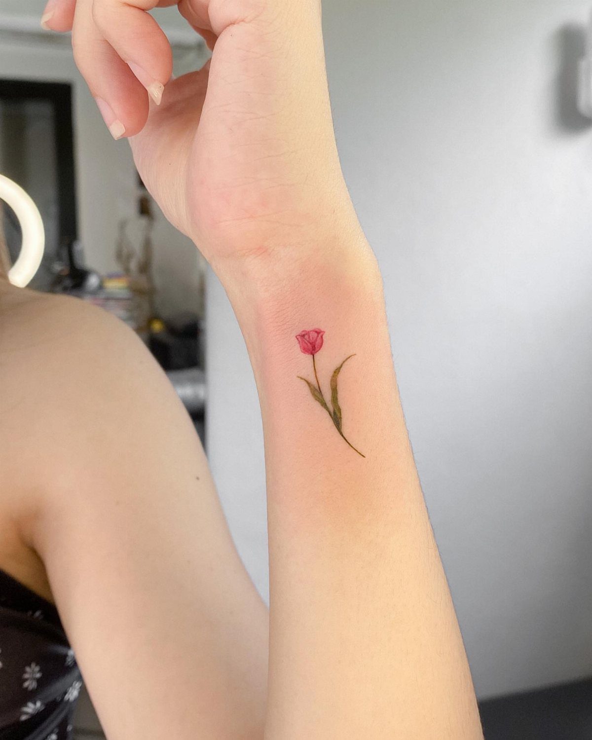 A small red tulip tattoo with a green stem on a person's forearm.