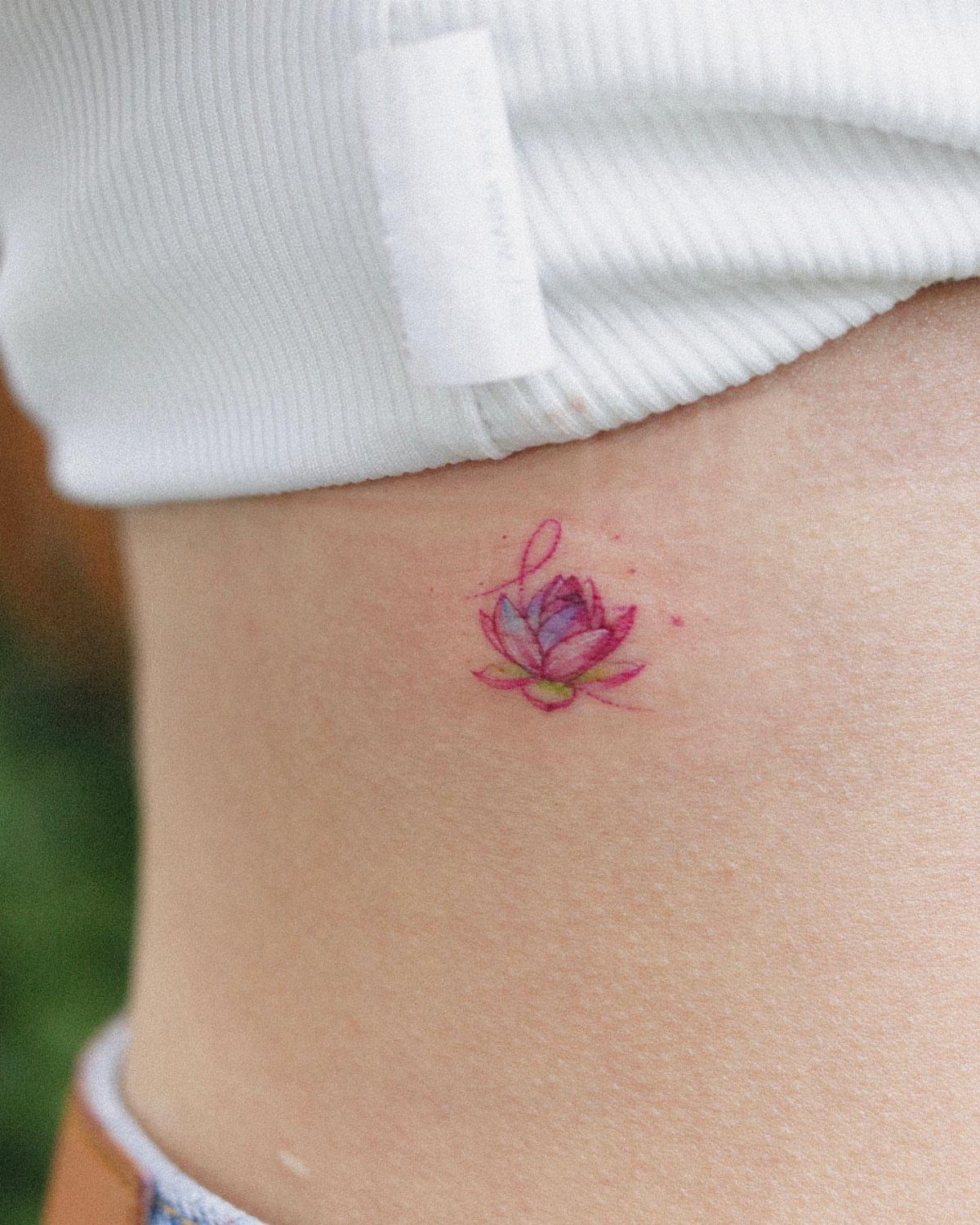 A small pink lotus flower tattoo on a person's hip skin.