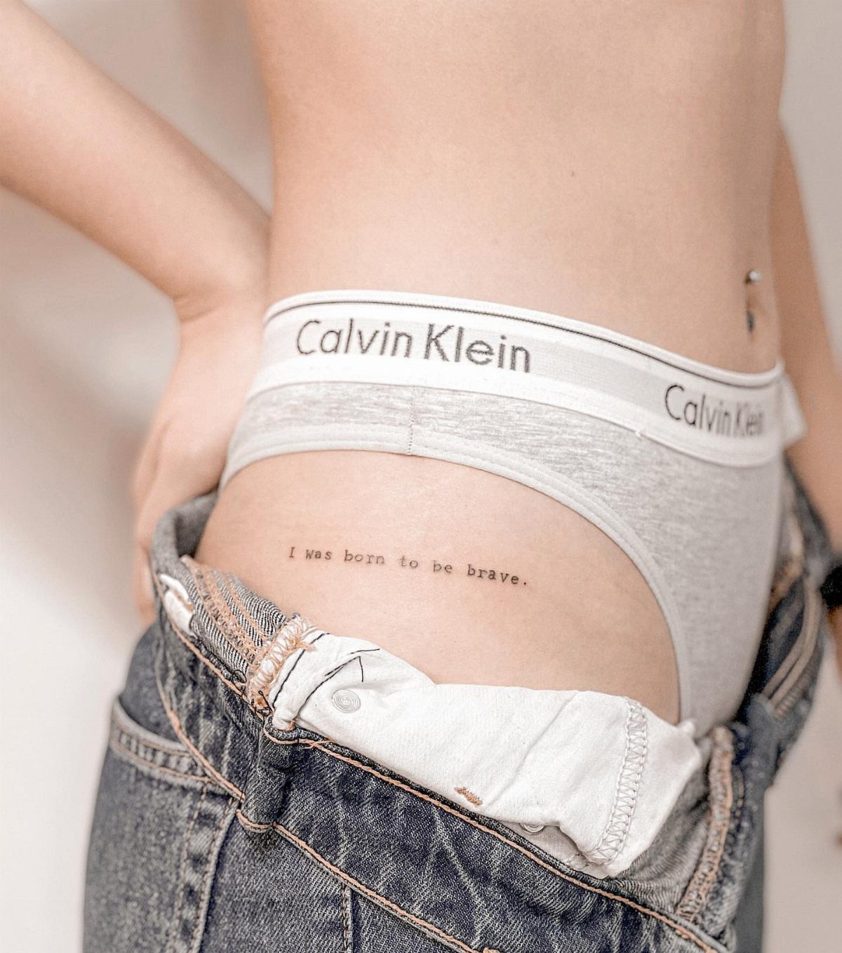 A small text tattoo on a person's hip reading I was born to be brave.