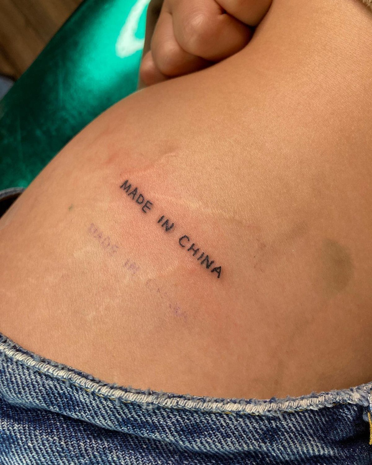 A small black text tattoo reading 'MADE IN CHINA' on a person's hip skin.
